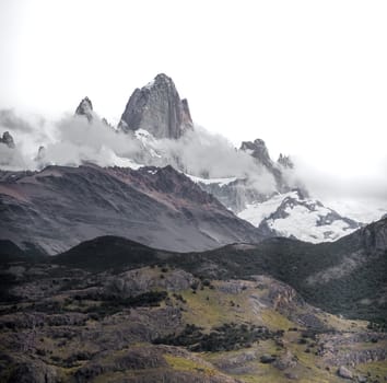 Tranquil mountain scenery featuring a lofty peak shrouded by soft clouds.