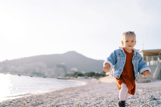 Little girl walks along a pebbly beach near the sparkling sea. High quality photo