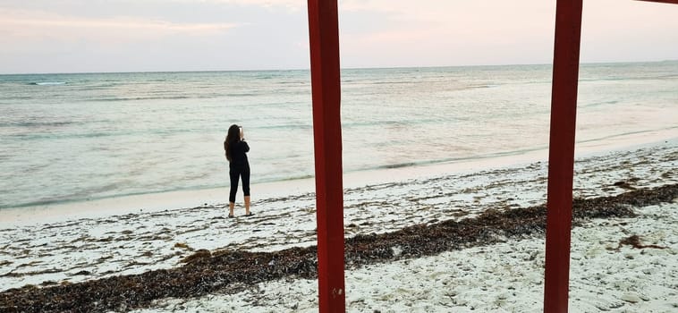 Shot of the woman by the sea shore with the cell phone, at sunrise hour