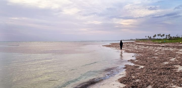 Shot of the woman by the sea shore with the cell phone, at sunrise hour