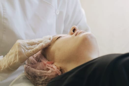 A woman lying down with eyes closed as a therapist massages her face using gentle and soothing motions.