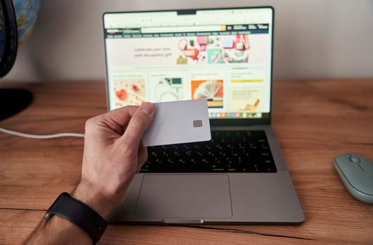 A person is holding a credit card in front of a personal computer with a laptop screen. They are using the touchpad to make a gesture