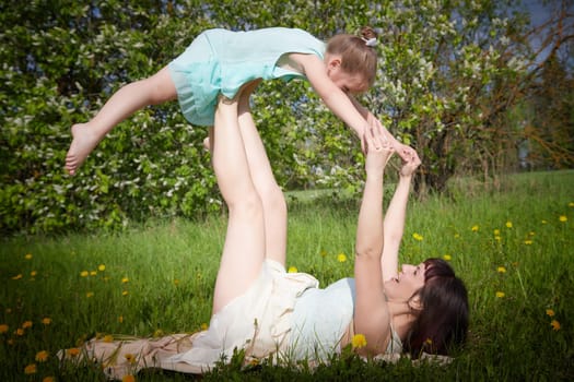 Happy mother and daughter enjoying rest, playing, fun and doing sports exercises on nature in a green field. Woman and girl resting outdoors in summer and spring day