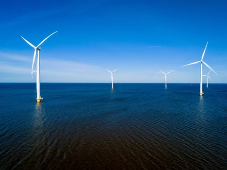 A group of wind turbines gracefully spin above the surface of the ocean in the Netherlands Flevoland during the vibrant season of Spring. drone aerial view of windmill turbines green energy