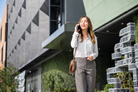Asian business female calling on smart mobile phone and walking on street outside office building, Happy businesswoman talking on smartphone outdoor in city with client, business communication