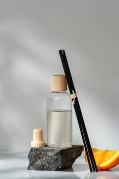 A reed diffuser with sleek black reeds is elegantly placed on a natural stone base beside a fresh slice of orange, creating an inviting and fragrant atmosphere. The translucent amber bottle catches the light, highlighting the essential oils within.