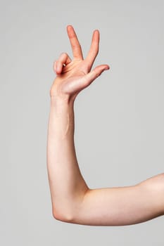 A single human arm is raised, captured in profile with the elbow bent and the hand slightly curved. The arms soft lighting emphasizes its form against the plain, unadorned backdrop.