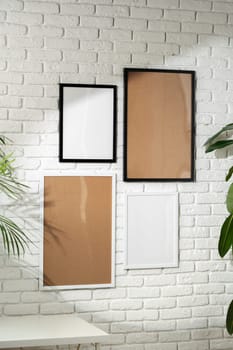 Several empty photo frames of different sizes and colors are displayed in an asymmetrical arrangement against a textured white brick wall, potentially signifying a modern and minimalist interior design approach. A small portion of a green plant is visible, injecting a touch of nature into the scene.