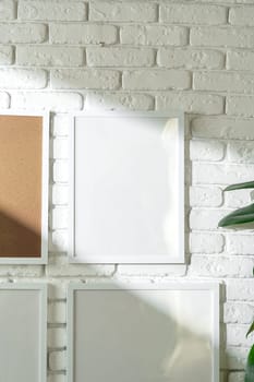 Several empty photo frames of different sizes and colors are displayed in an asymmetrical arrangement against a textured white brick wall, potentially signifying a modern and minimalist interior design approach. A small portion of a green plant is visible, injecting a touch of nature into the scene.