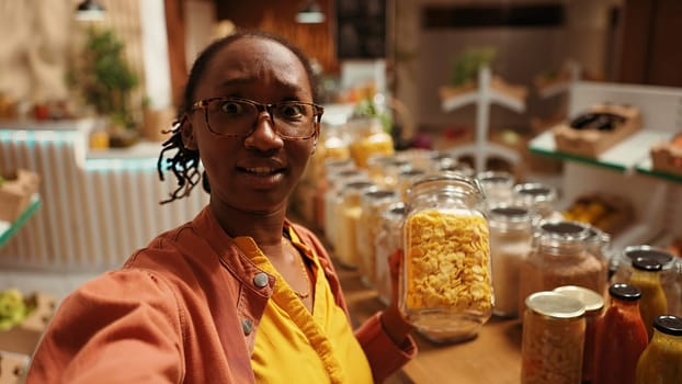POV of african american client promoting local bio supermarket on social media networks, filming video online to create ad. Woman presenting additives free bulk items and produce. Handheld shot.