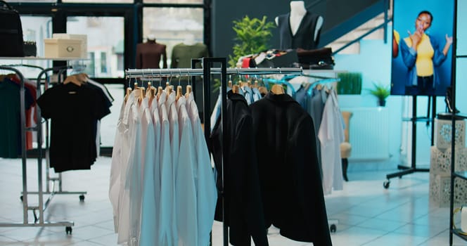 Empty trendy clothing store selling fashionable items and shoes, filled with new casual or formal merchandise. Shopping center boutique having fashion collection on racks, bags on display. Camera B.