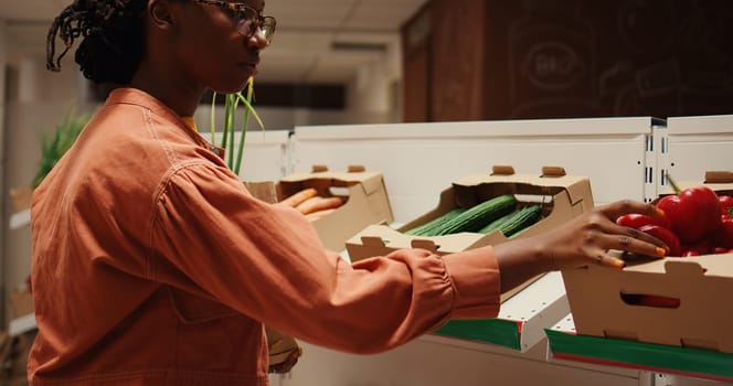 African american buyer choosing organic produce from crates, putting fruits and veggies in a paper bag to purchase. Woman shopping for natural eco friendly products at local farmers market. Camera 2.