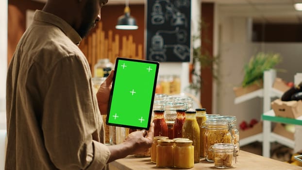 African american client holding tablet with greenscreen layout in local organic shop, looking at chromakey next to additives free goods. Regular customer uses device with isolated copyspace. Camera 1.