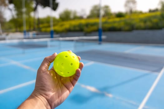 Close-up of a hand holding pickleball yellow ball in an outdoor court
