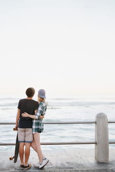 Couple, rear view and hug on beach for travel with mockup space, adventure and promenade date. Gen z skater, people and skateboard on boardwalk for bonding, embrace and outdoor fun with morning waves.