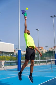 Vertical photo of a young african sportive man jumping playing pickleball outdoors