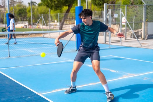 Full length photo of a young man hitting the ball playing pickleball outdoors