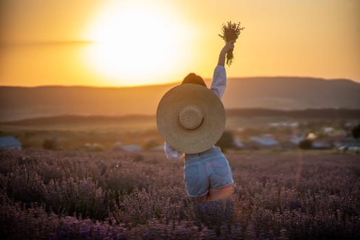 Woman lavender field sunset. Back view woman in a white blouse, denim shorts and hat. Aromatherapy concept, lavender oil, photo session in lavender.