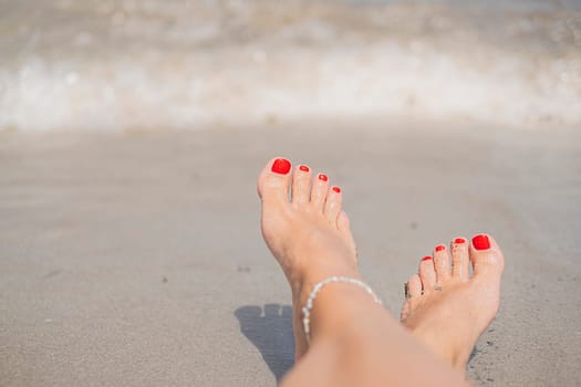Vacation holidays. Woman feet closeup with red painted nails of girl relaxing on beach on sunny summer day.