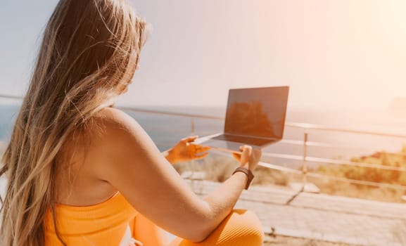 Digital nomad, Business woman working on laptop by the sea. Pretty lady typing on computer by the sea at sunset, makes a business transaction online from a distance. Freelance, remote work on vacation