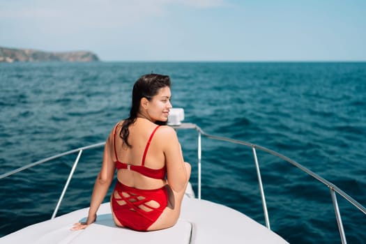 Yacht woman in a red bikini posing while on the bow of a yacht. Happy woman is sunbathing on the bow of a ship during a boat trip. Travel concept, vacation at sea.