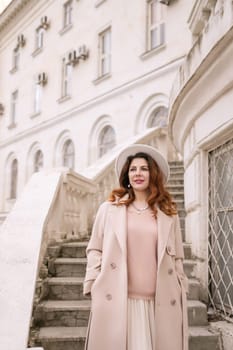 woman in elegant coat and hat against an intricate architectural backdrop, harmoniously blending modern fashion with historical allure. The soft daylight adds to its timeless appeal