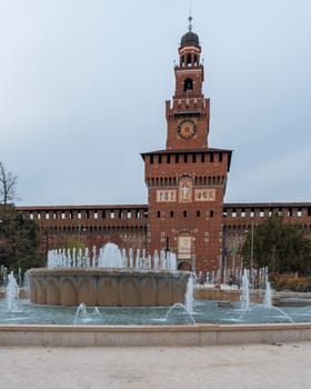 Nice view of main entrance to the Sforza Castle - Sforzesco castle and fountain in front of it, overcast day,Milan, Italy.
