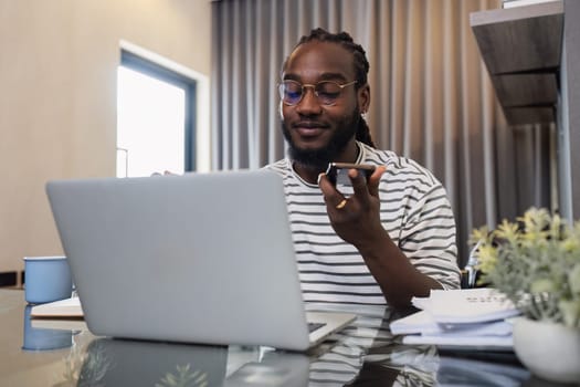 Young African American business man working with laptop and document on desk and talking on mobile at home.