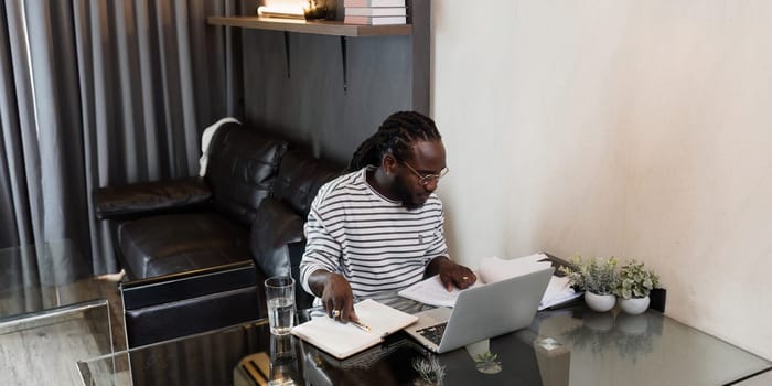 Young African American business man working with laptop and document on desk at home. work from home concept.