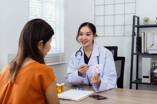 A woman is sitting at a desk with a doctor. The doctor is holding a pill and is explaining it to the woman. The woman is smiling and seems to be happy with the explanation
