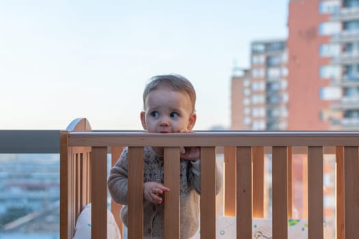 Baby in a crib against the backdrop of tall city buildings. Urban environment concept.
