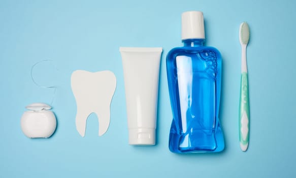 Mouthwash, toothpaste tube, dental floss on a blue background, oral hygiene, flat lay