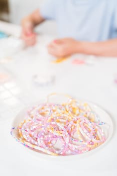 Little girl enjoys crafting colorful bracelets with vibrant clay beads set.