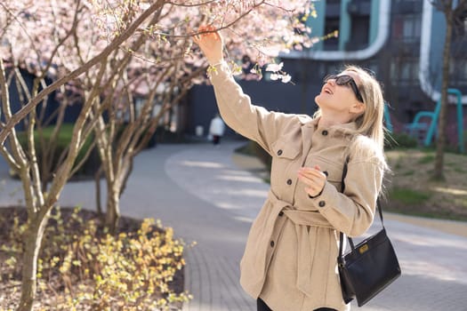 Blonde touches a branch of blooming cherry standing in the park. High quality photo