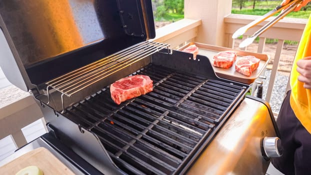 The outdoor two-burner gas grill is put to good use, sizzling with the sound and aroma of ribeye steaks and onion rings being perfectly cooked.