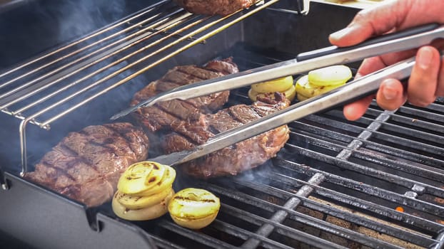 The outdoor two-burner gas grill is put to good use, sizzling with the sound and aroma of ribeye steaks and onion rings being perfectly cooked.