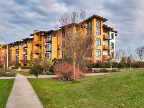 Concrete pathway across green lawn in front of residential condo building. Residential apartment building on cloudy day with overcast sky.