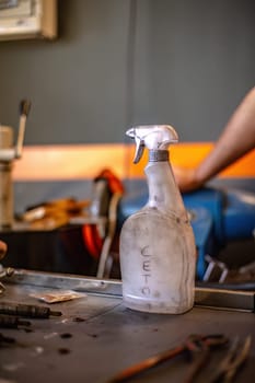 A grimy spray bottle sits in a workshop, a testament to frequent use in vehicle maintenance.
