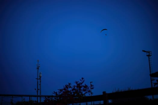 A lone paraglider drifts above urban structures against the tranquil twilight sky.