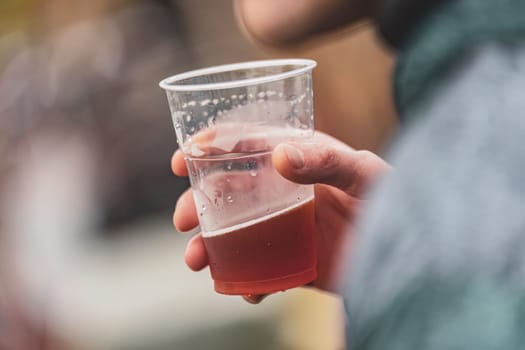 Close-up view of a hand gripping a plastic cup filled with beer, symbolizing casual outdoor drinking.