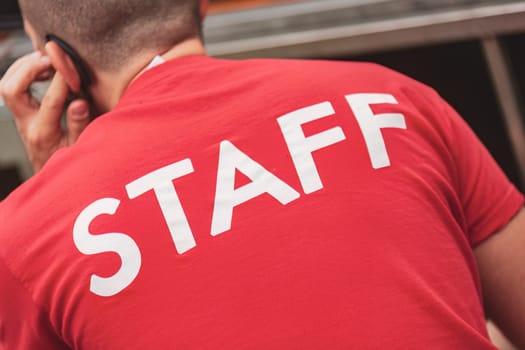 A man wearing a red staff shirt is actively engaged in a phone conversation.