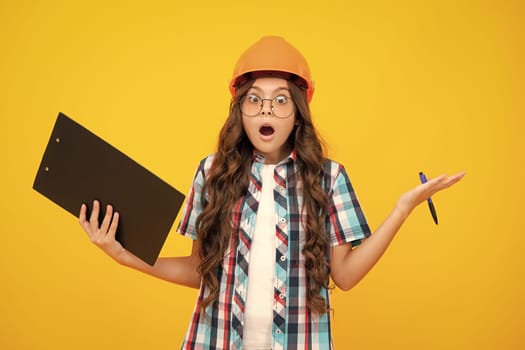 Shocked surprised teenager girl. Teenager child painter in helmet with clipboard. Child in hard hat. Kid engineer on construction site. Renovation and repair