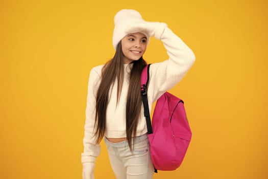 Back to school. Teenager schoolgirl with warm hat and sweater on yellow isolated studio background. Winter school