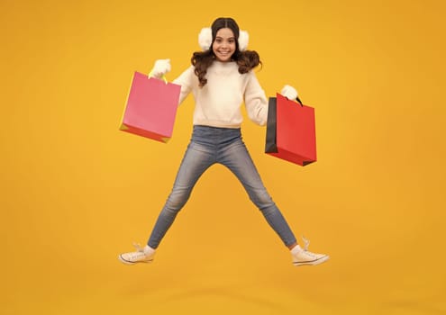 Girl teenager with shopping bags isolated on yellow backgound. Shopping and sale concept. Excited teenager girl. Run and jump