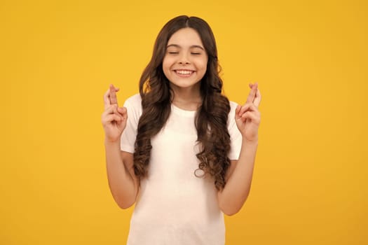 Teenager child girl crossing her fingers and wishing for good luck, isolated on yellow studio background with copy space