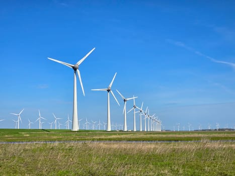Windmill park in the meadow during spring, view of windmill turbines on a Dutch dike generating green energy electrically, windmills isolated at sea in the Netherlands.