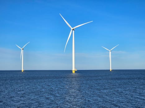 Windmill park in the ocean, view of windmill turbines on a Dutch dike generating green energy electrically, windmills isolated at sea in the Netherlands. Energy transition