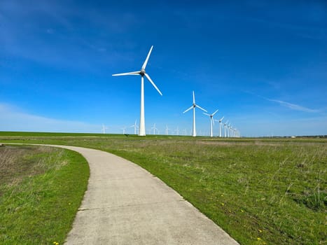 Windmill park in the green meadow in Spring, view of windmill turbines on a Dutch dike generating green energy electrically, windmills isolated at sea in the Netherlands.