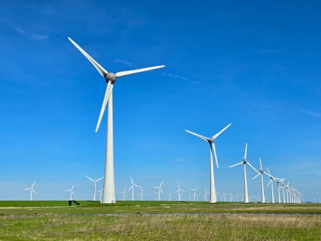 Windmill park in the meadow with a blue sky, view of windmill turbines on a Dutch dike generating green energy electrically, windmills isolated at sea in the Netherlands.