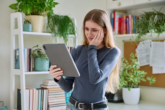 Young teenage female student at home looking talking in web camera of digital tablet. Girl teenager 16,17,18 years old studying remotely, video conference call, e-learning technology education